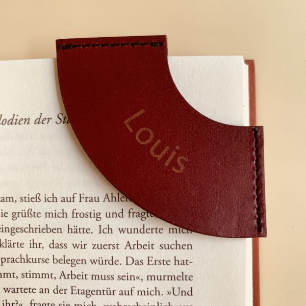 Rotes Lesezeichen aus Leder. Das Lesezeichen ist auf eine Buchseite gesteckt.